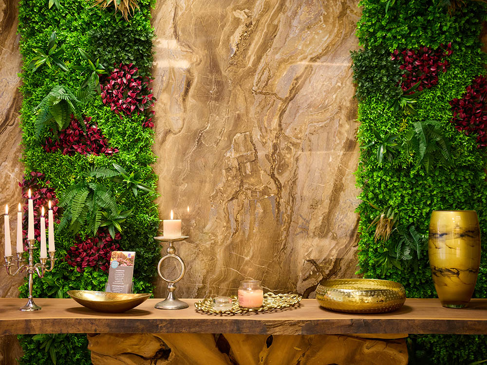 Bestattungsvorsorge – Dekorationskonsole mit Kerzen & Urne Naturholz-Konsole mit Kerzenständer, goldener Urne und Dekoration vor vertikaler Grünwand – Symbolfoto zur Bestattungsvorsorge in Versmold.
